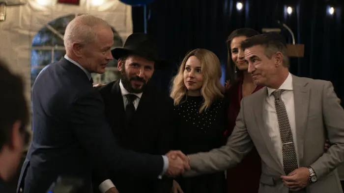 Rabbi Mo and community leaders share a tense handshake at a formal evening gathering in Guns & Moses