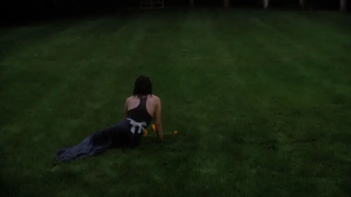 Grace lies alone in a dark dress on a vast green lawn in Fractals