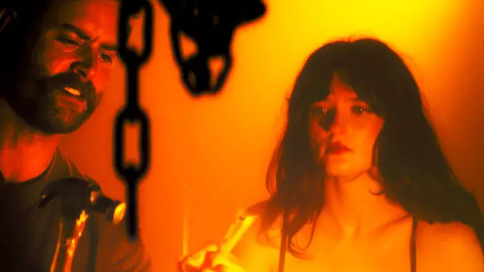 Amy and Seth bathed in eerie orange light, surrounded by chains in a nightmare sequence from No Choice.