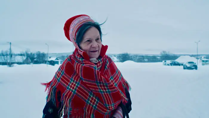 Elder Sami woman in traditional dress stands against a snowy landscape in The Tundra Within Me