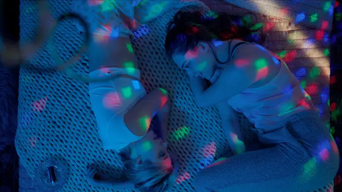 Molly and Irene lying on the bed under colorful lights in Upon Waking