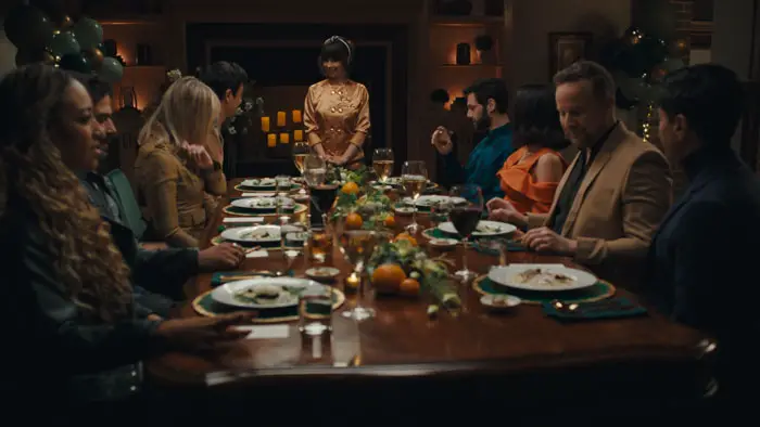 Guests sit around a dinner table as a chef stands at the head in Nuked