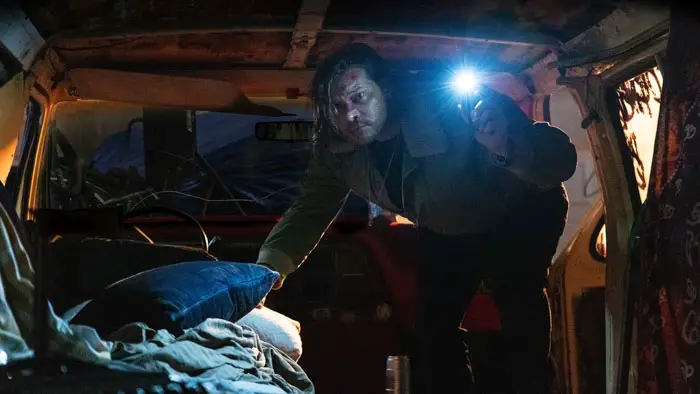Zebedee Row as CB searching a dimly lit van with a flashlight in Invisible