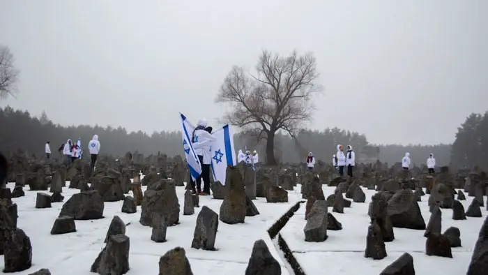 Israeli students stand with flags among memorial stones at a Holocaust site in Delegation.