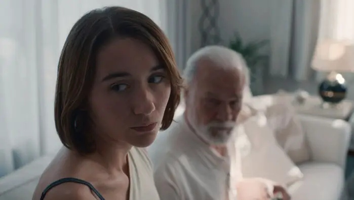 Cata sits with her grandfather in a quiet, somber moment from Forastera.
