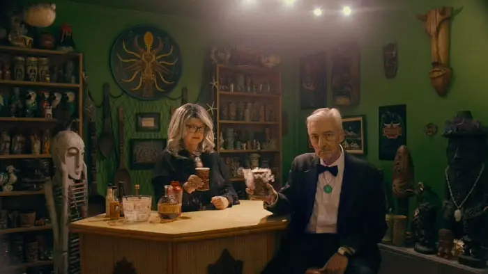 Two older Satanist church members sharing drinks inside a tiki-themed home bar