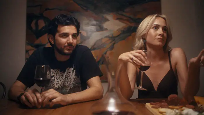 A man and woman sitting at a dinner table with wine in Rent Free