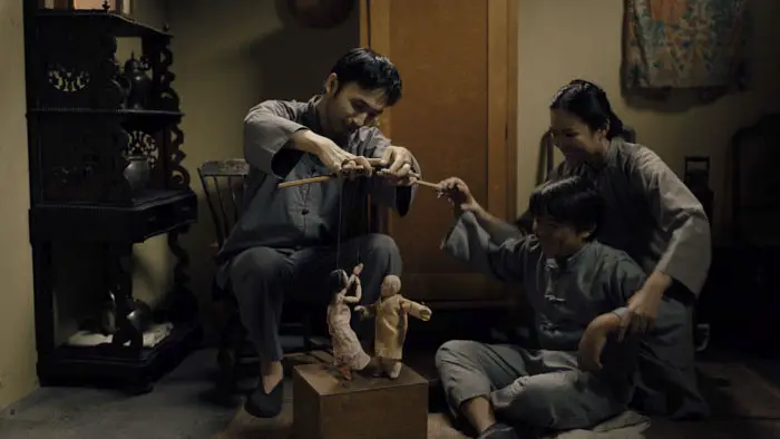 A Chinese family plays with puppets in a warm, dimly lit room in Site.