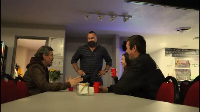 Cast members sitting around a table talking in a scene from Vampire Clown