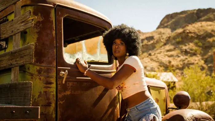 Dazelle Yvette as Mama Birdy stands beside a rusty truck in the desert in Brute 1976.