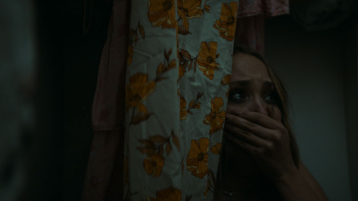 Evie (Reese Ravencraft) hides in fear behind floral curtains in Reset (2025). 
