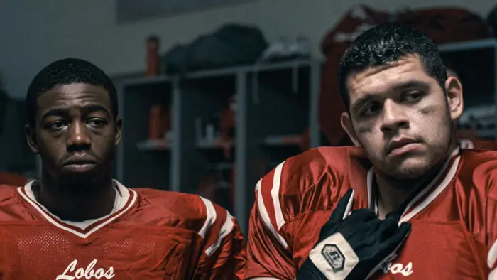 Two football players sit in the locker room wearing Lobos jerseys in The Senior.