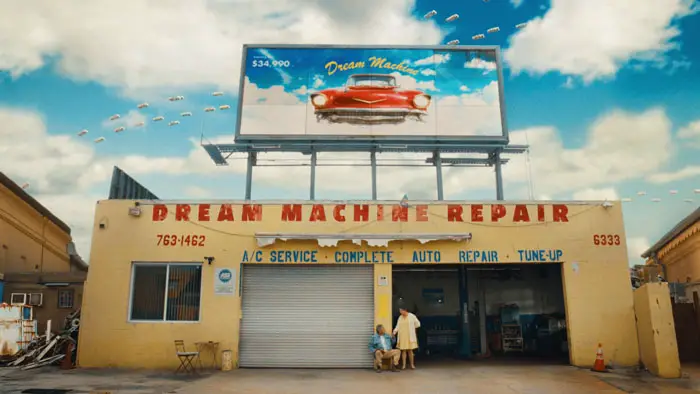 Marco and Isabela outside Dream Machine Repair auto shop beneath a billboard advertising flying cars.