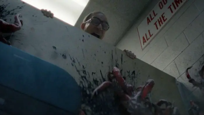 A terrified man looks down as red alien vines burst through a wall, splattering black goo. 