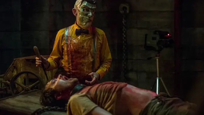 Jackie Earle Haley stands over David Angland in a violent scene from Your Host, surrounded by chains and industrial lighting.