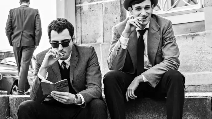 Guillaume Marbeck and Aubry Dullin as Jean-Luc Godard and Jean-Paul Belmondo sit on Paris steps smoking and reading in Nouvelle Vague.