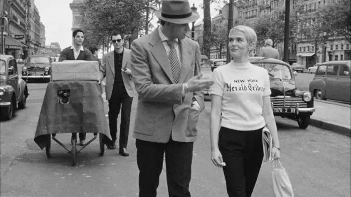 Zoey Deutch as Jean Seberg walks through Paris in Nouvelle Vague wearing a New York Herald Tribune shirt.