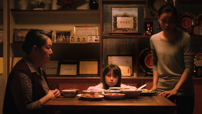 Anna sits at the dinner table between her grandmother and caregiver in Runaway Sisters