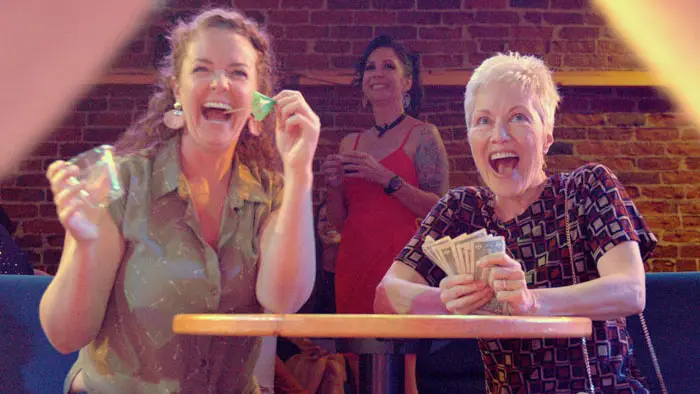 Priscilla Quinby and Stephanie C. Jones laugh and hold cash during a lively bar scene in The Eve of May.