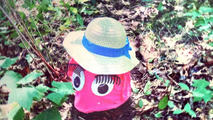 Pink puppet character wearing a straw hat in a forest clearing.