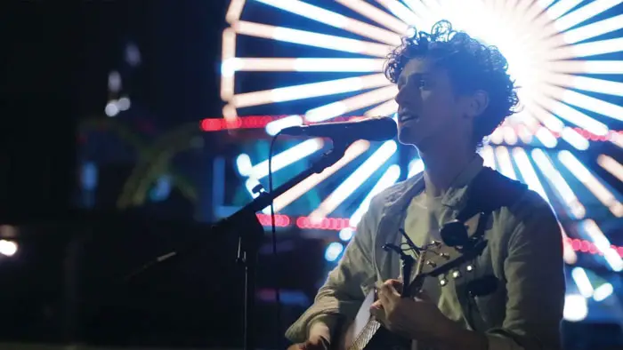Street performer singing and playing guitar on stage in front of bright lights