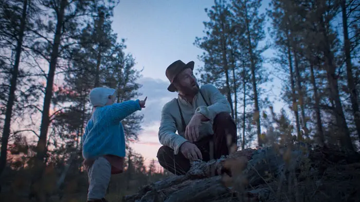 Robert Grainier with his young child in the forest at dusk in Train Dreams