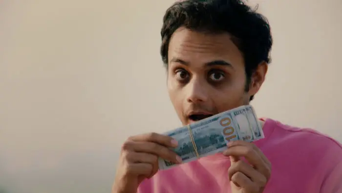 Ushmey Chakraborty as Ravi holding a stack of hundred-dollar bills in Gay, Asian, Immigrant