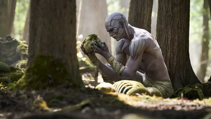The Creature examines a skull in the forest in Guillermo del Toro’s Frankenstein (2025).
