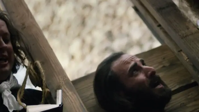 Man positioned beneath the guillotine during an execution scene in Guillotine (2025).