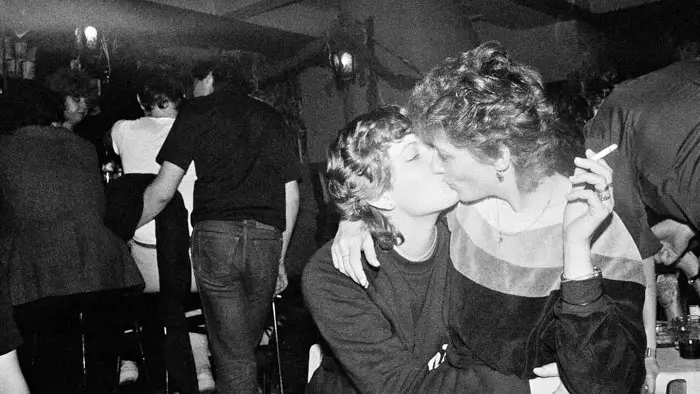 Two women kissing in a crowded bar in a black-and-white photograph by Libuše Jarcovjaková.