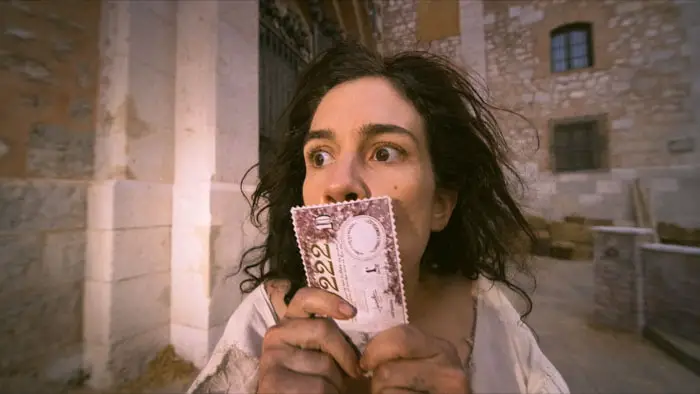 A woman clutching a lottery ticket with a shocked expression in Mariana Hormiga.