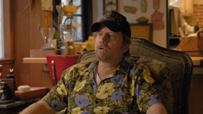 Jamie Kennedy sitting in a Hawaiian-themed room wearing a floral shirt and hat in Namaka