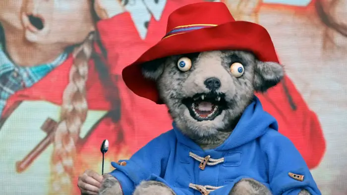 Parody version of Paddington Bear on Spitting Image wearing a red hat and blue coat.