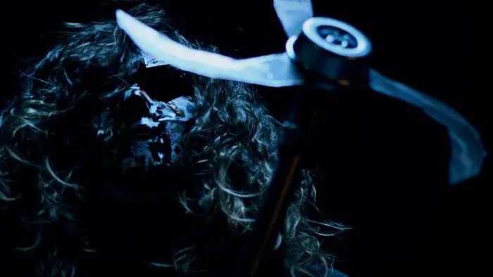 A masked killer wields a bladed farming tool in a dark scene from The Weed Hacker (2025)