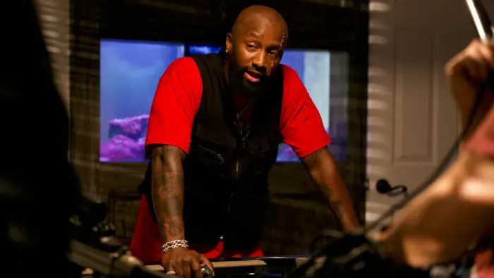 A gang leader stands over a table of weapons during a tense moment in Armstrong: Dark Secrets.