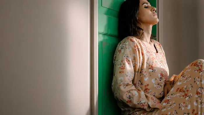 A woman sits against a green wall in a quiet, contemplative moment from BAAB (2025)