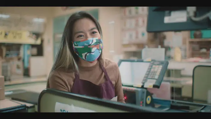 Stacy Chu as Amy working behind the counter at a grocery store during the COVID lockdown in Essentially Amy.