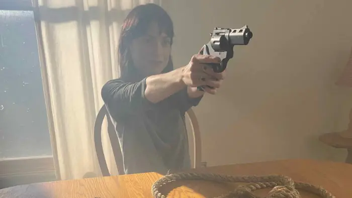 Debbie aims a revolver while seated at a table in Half Dead Fred