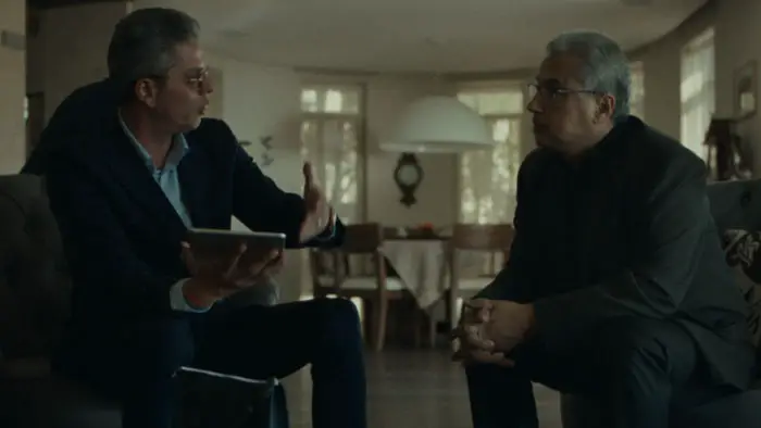 Two older men meet in a living room discussing a serious family matter in Happy Holidays (2025).