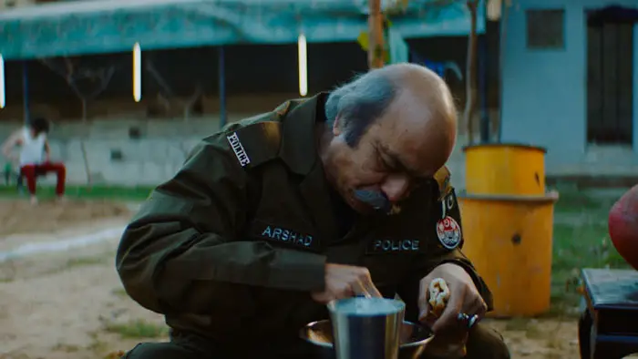Officer Arshad eating during a quiet moment outdoors in the film Jujji. 