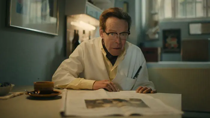 Ole Benny sits at a small table reading the newspaper in Just the Usual. 