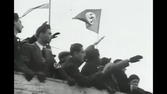 Archival black-and-white footage of a Nazi rally with salutes and swastika flags.