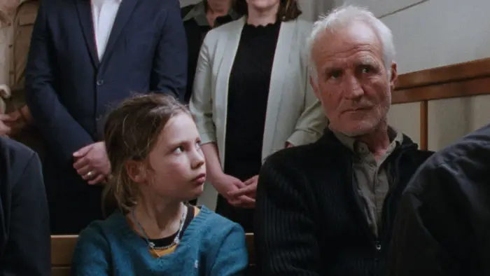 Johan sits beside his granddaughter in a crowded courtroom in a scene from Reedland.