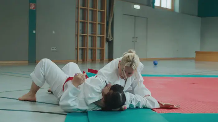 Close-up of two women in karate gis locked in a grip during an intense sparring moment in Slugfest (2025).
