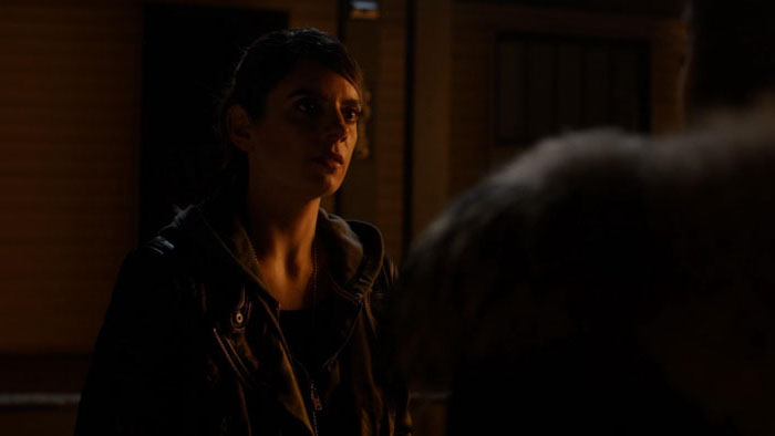 A woman in a leather jacket looks up tensely in a dim room in Super Happy Fun Clown (2025). 