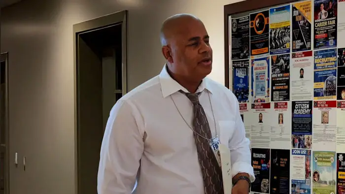 An FBI agent speaks inside a hallway lined with recruitment posters in The Hunger. 