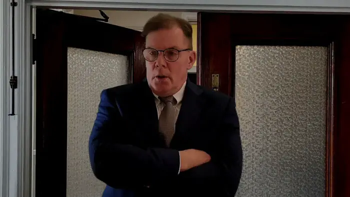 A suited man stands in a doorway with folded arms during an investigation scene in The Hunger.