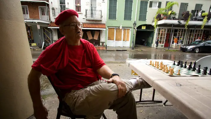 Jude Acers sits at his street chess table in New Orleans wearing his signature red beret