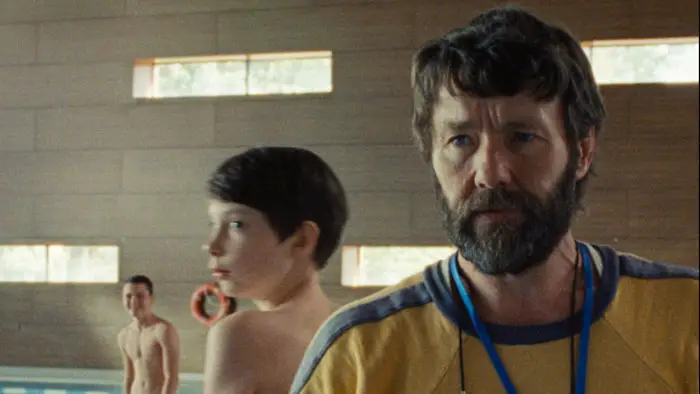 Joel Edgerton as the camp coach standing poolside while the boys train in The Plague (2025).