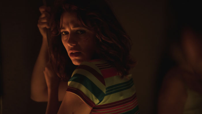 Malena Villa as Camila hiding in low light with a fearful expression in The Wailing (2025).